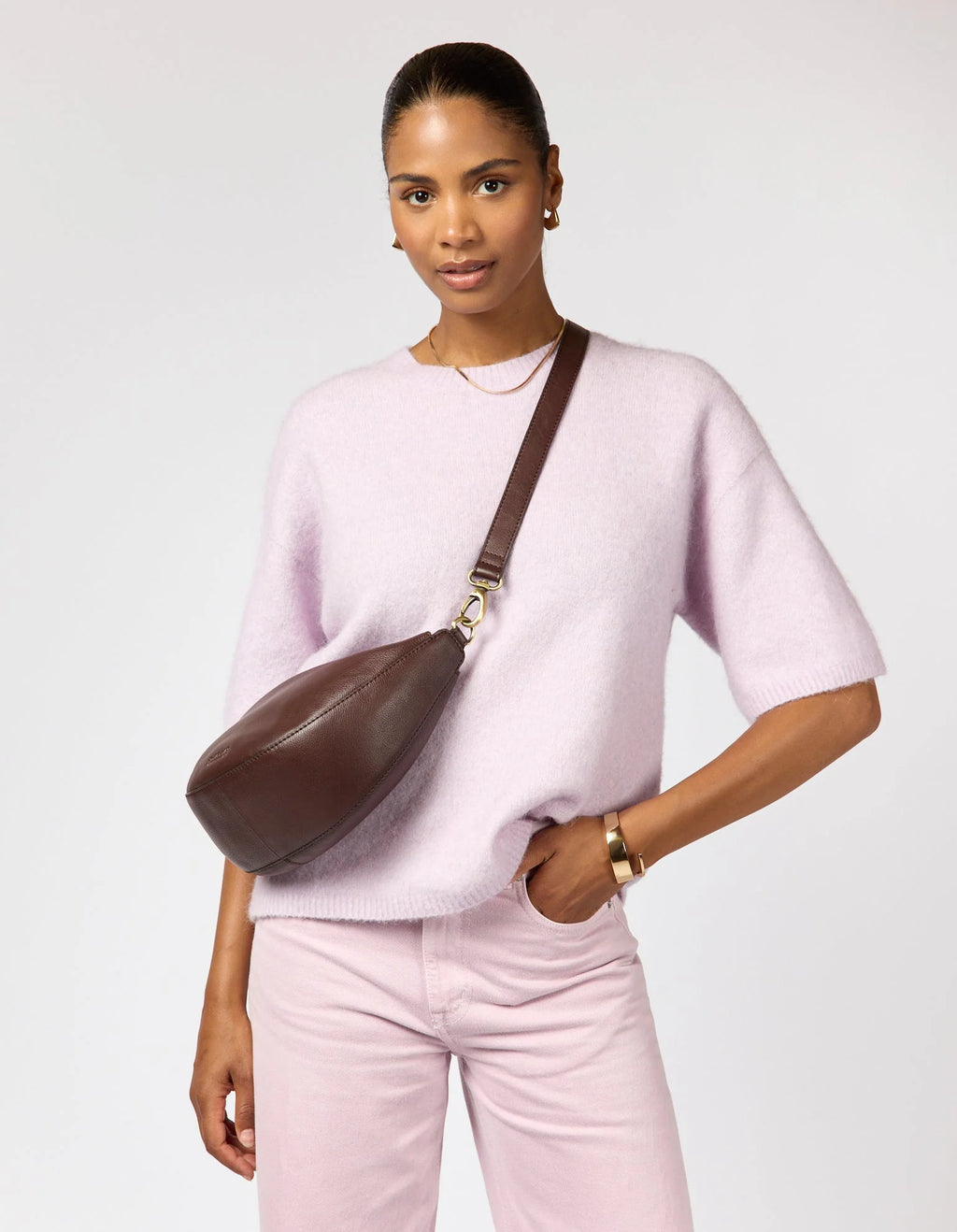 Woman wearing a pink sweater and pants with a brown leather crossbody bag on a white background