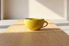 Yellow mug on a wooden table with sunlight casting shadows