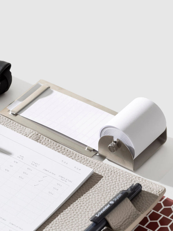 Notebook with pen and paper roll on a white surface next to a task roller
