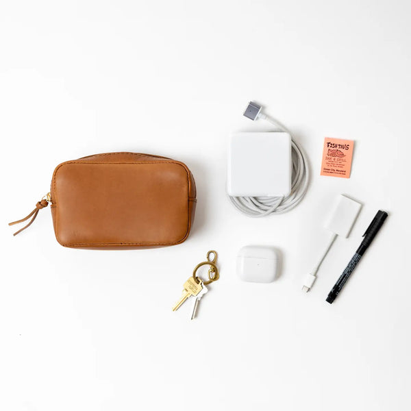 Brown leather pouch with keychain, white power adapter, and black pen on a white background