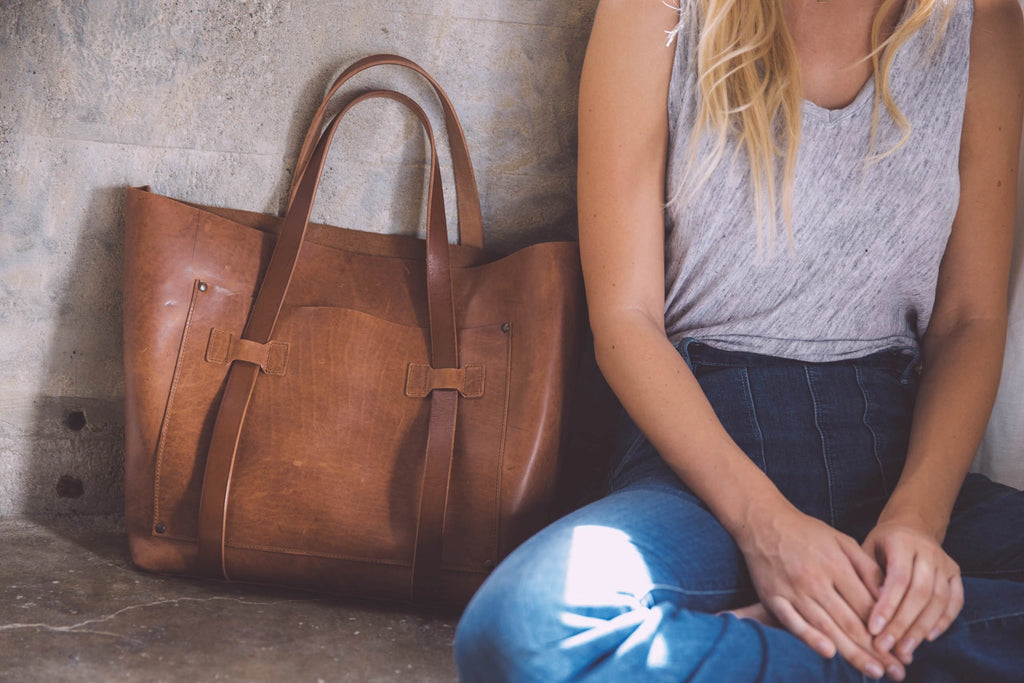 Brown leather tote bag next to a person sitting on the ground.