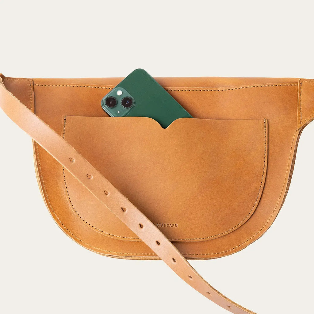 Brown leather bag with a green phone in the pocket on a light beige background