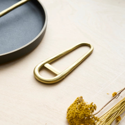 Gold bottle opener on a light surface with dried flowers and a blue ceramic dish.