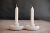Two white candles in ceramic holders on a wooden surface with a dark background