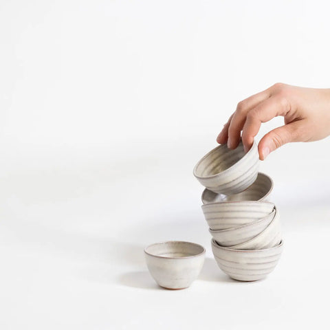 Hand interacting with a stack of ceramic bowls on a white background