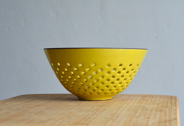 Yellow colander/berry bowl on a wooden surface with a gray background