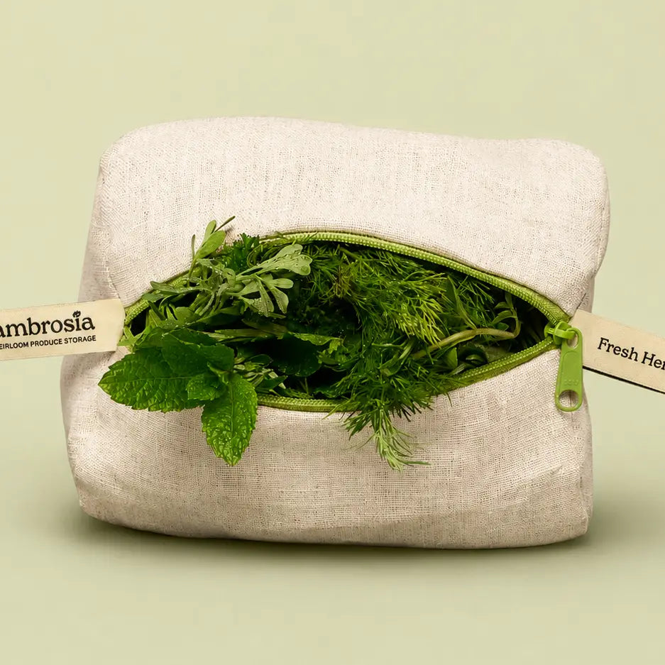 A square beige linen produce storage pouch with a green zipper opening, shown filled with fresh green herbs. Two paper tags are attached to the zipper, one reading 'Ambrosia' and the other partially visible as 'Fresh Herbs.