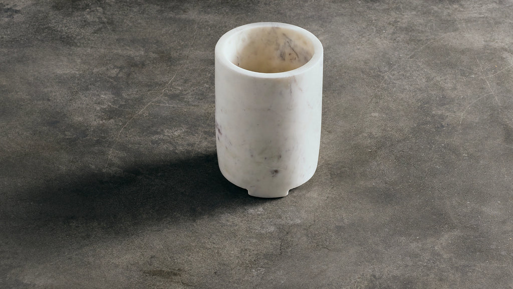 A small cylindrical white marble wine cooler made of natural marble, standing on a textured dark gray surface.