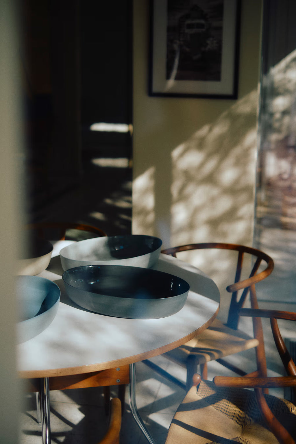 Dining area with a table and chairs, sunlight casting shadows on the floor.