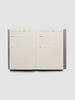 An open weekly planner notebook with lined pages for Monday through Sunday, photographed from above on a light gray background.