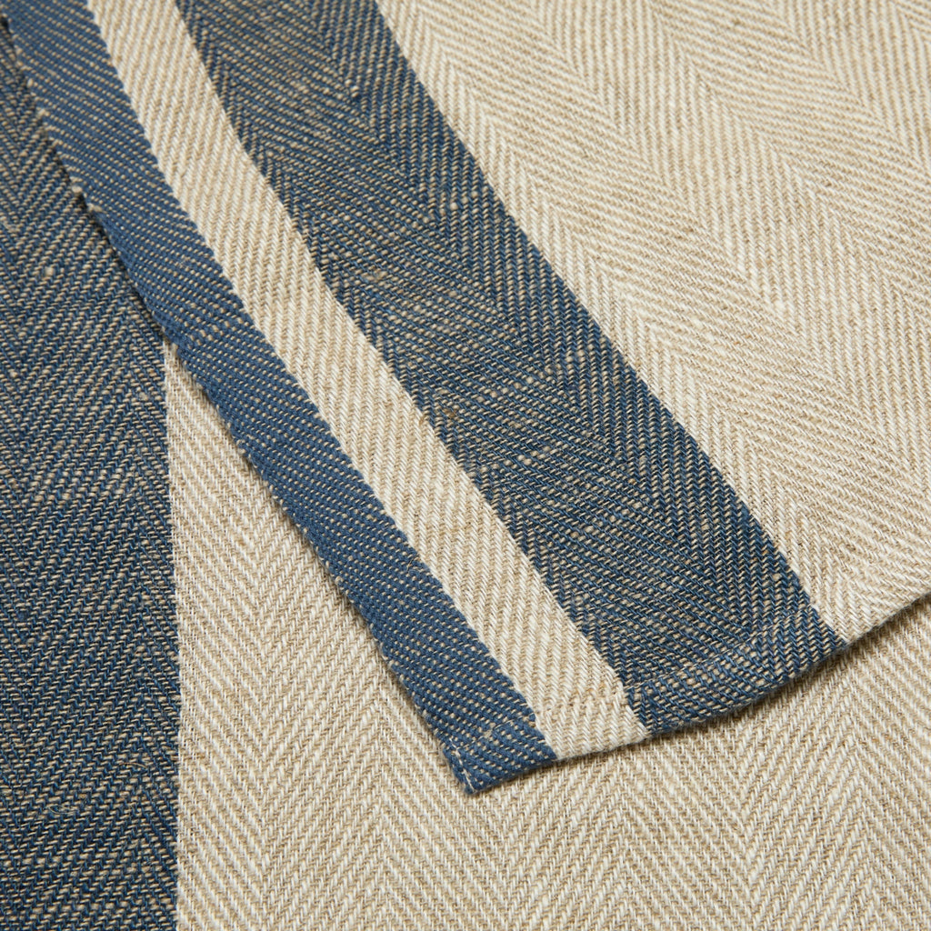 Close-up of a woven textile with a beige herringbone pattern and two vertical navy blue stripes.