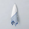 White towel with blue stripes and tassels hanging on a gray wall.
