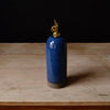 Blue ceramic oil bottle with gold cap on a wooden surface