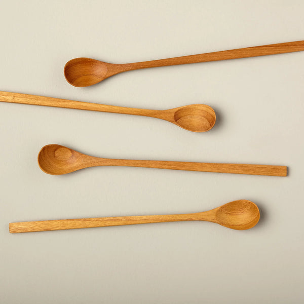 four spoons made out of teak wood on a flat surface. The background is a grey/beige color