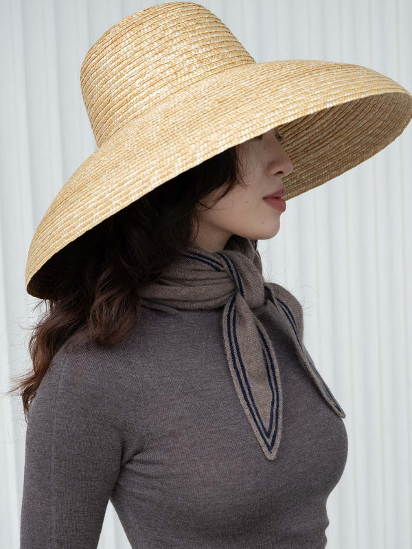 Person wearing a wide-brimmed straw hat and gray top with a scarf against a white background