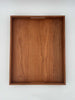 A rectangular wooden serving tray with a warm medium-brown wood grain finish and a small recessed handle cutout at the top edge, shown against a plain white background.