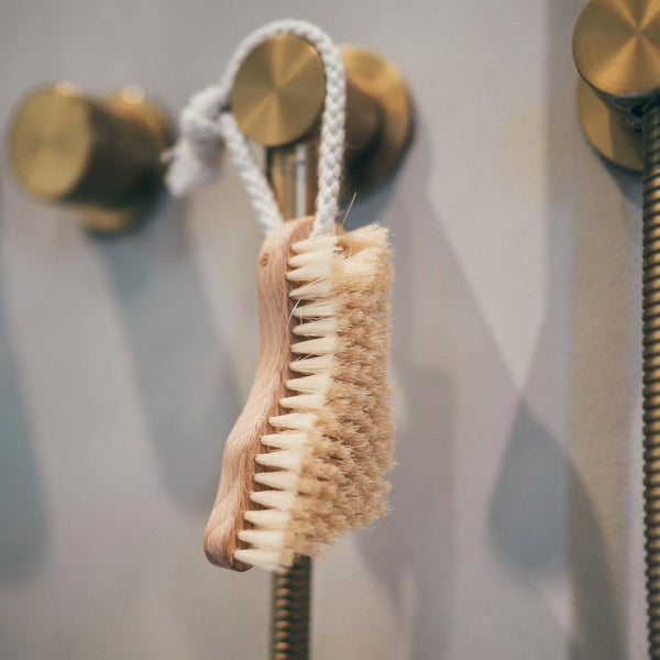 Brush with natural bristles hanging on a gold hook against a neutral background