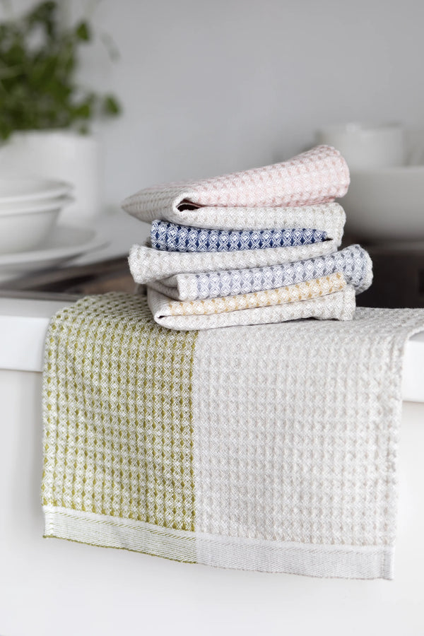Folded dishtowels in a stack on top of a dishtowel that is hanging - spread out.