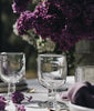 Clear glass goblets on a table with purple flowers in the background