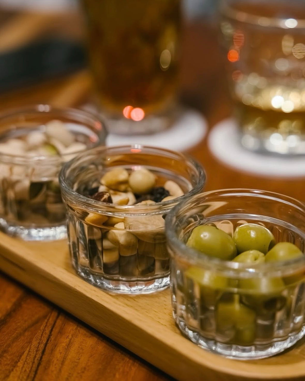 Three small glass containers with snacks on a wooden tray.