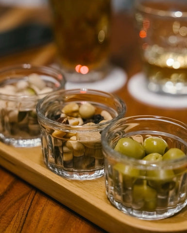 Three small glass containers with snacks on a wooden tray.