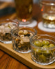 Three small glass containers with snacks on a wooden tray.