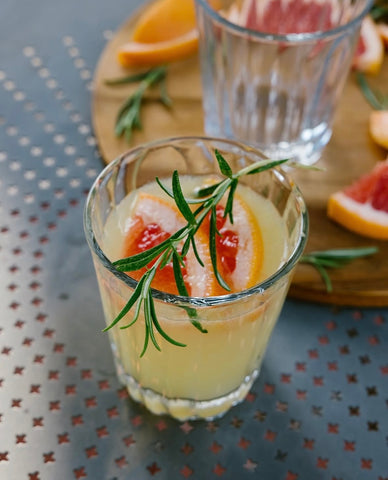 Glass of lemonade with grapefruit slices and rosemary on a textured surface