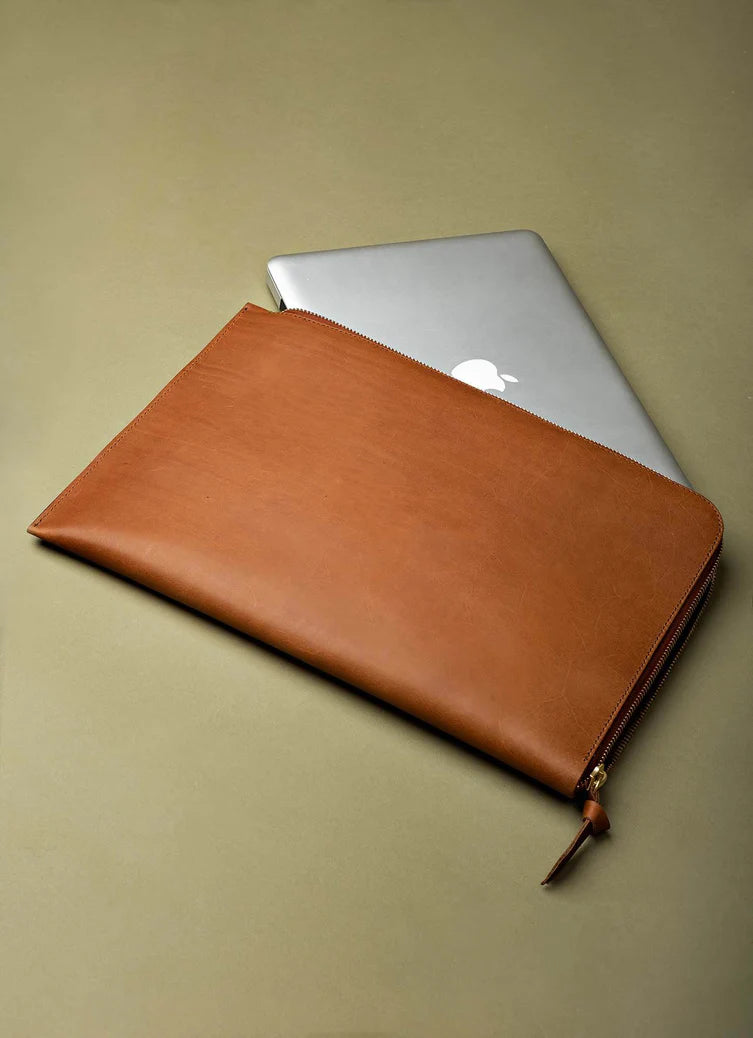Brown leather laptop sleeve with a silver laptop on a beige background