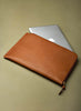 Brown leather laptop sleeve with a silver laptop on a beige background