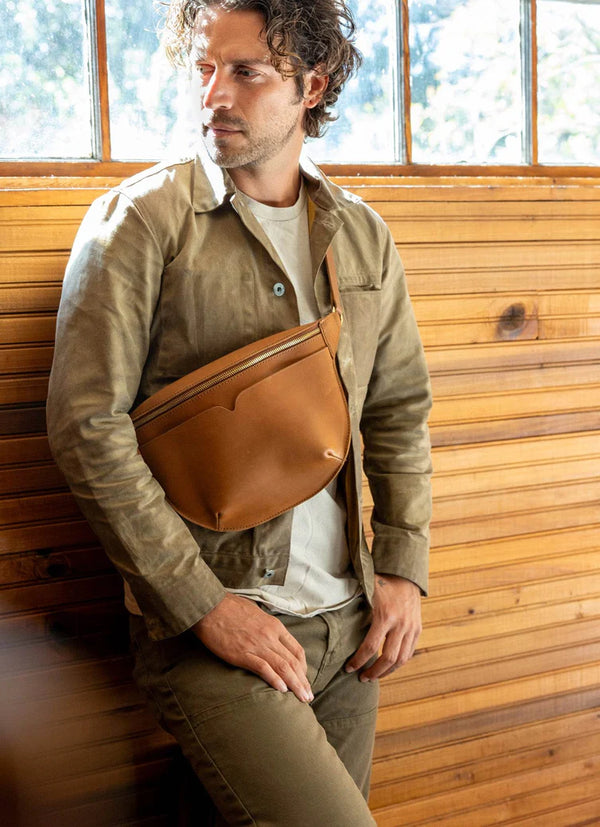 Man wearing a brown leather bag against a wooden wall