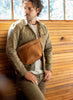 Man wearing a brown leather bag against a wooden wall