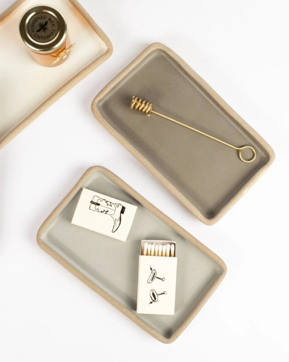 Two ceramic trays with decorative items including a bottle, matches, and a small tool on a white background.