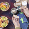 Person spreading a spread on a piece of bread with bowls of salad and a jar of spread on a table.