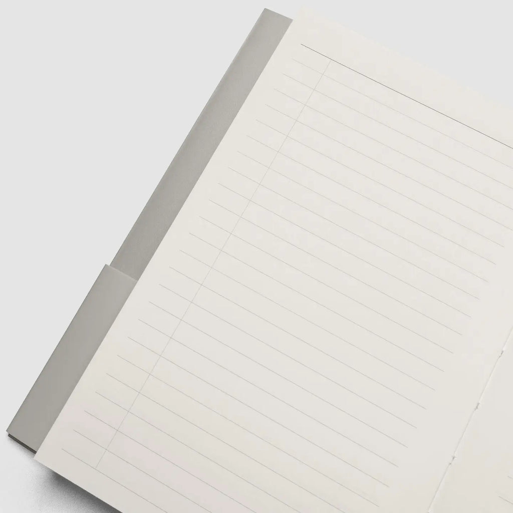 A close-up of an off-white lined notepad or memo pad with a gray cover or backing, photographed on a light gray background.