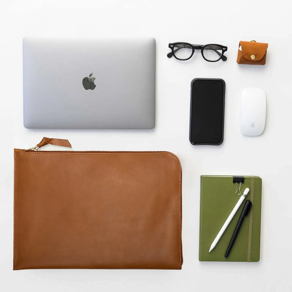 Collection of office items including a laptop, phone, mouse, glasses, and a leather pouch on a white background.