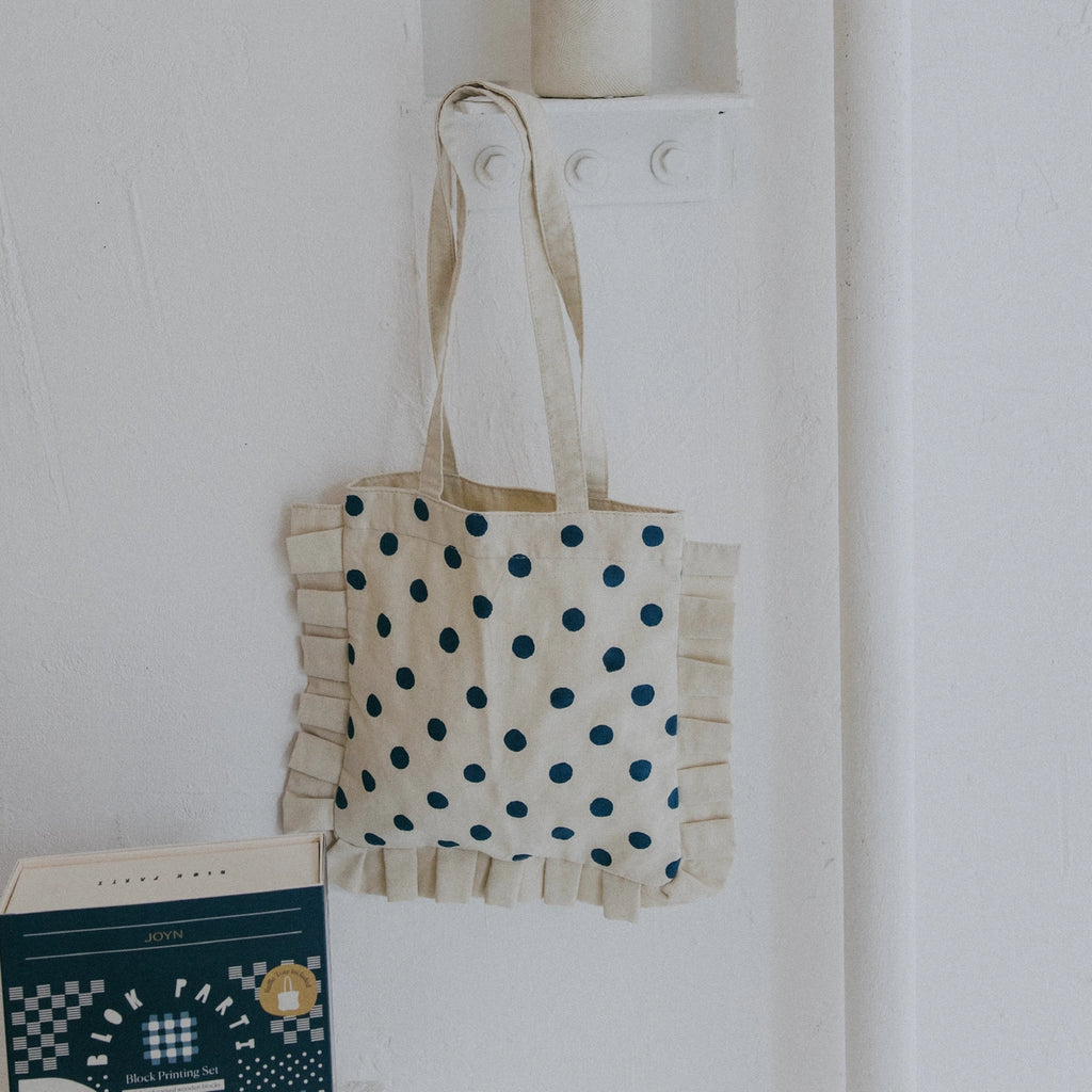 Tote bag with blue polka dots hanging on a white wall next to a book.