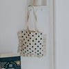 Tote bag with blue polka dots hanging on a white wall next to a book.