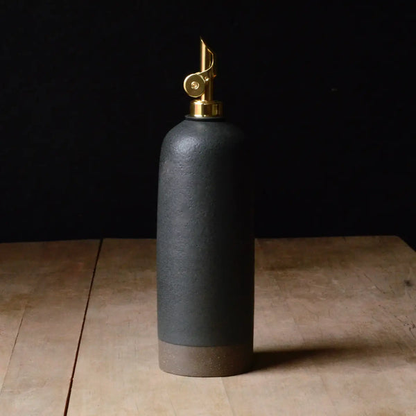 Black ceramic bottle with gold cap on a wooden surface