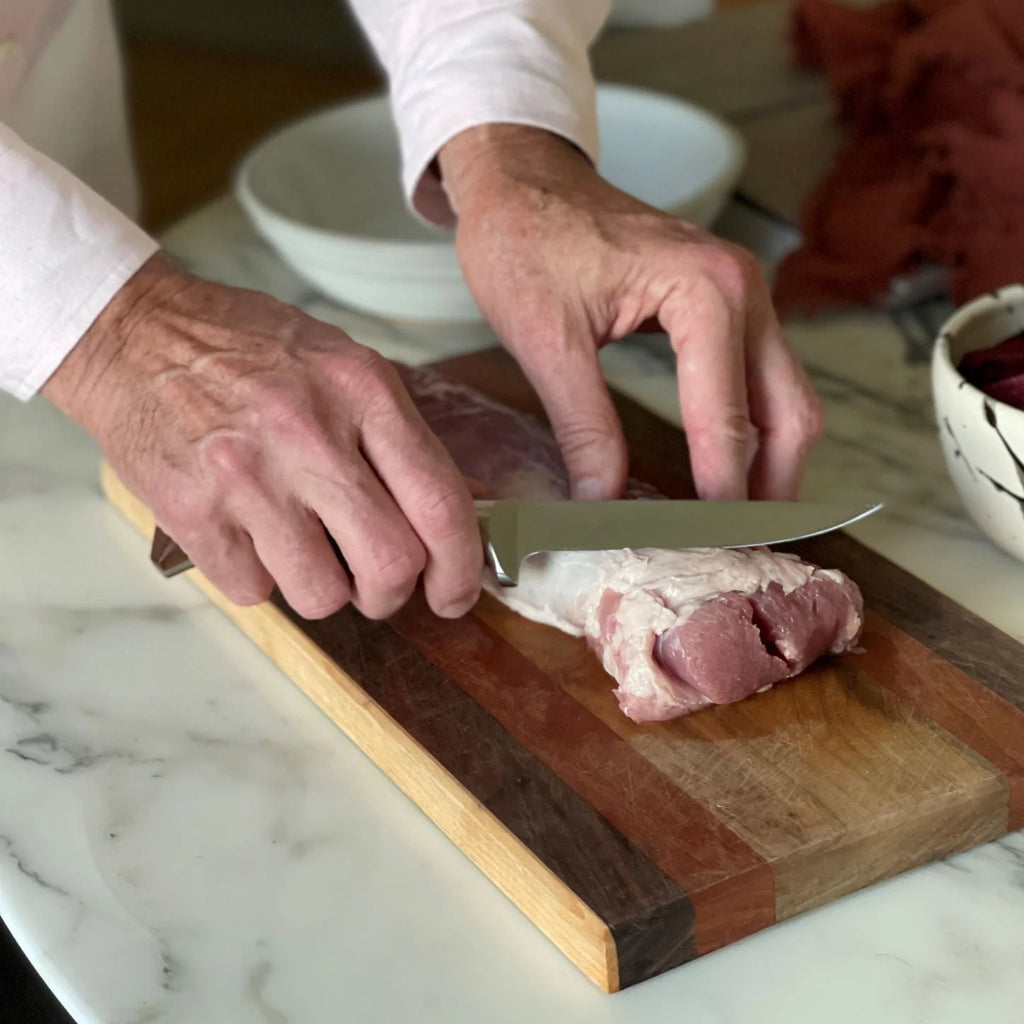 Person cutting meat on a wooden cutting board with a white plate in the background