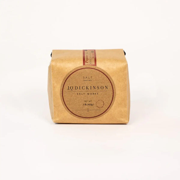 A square kraft paper package of JQ Dickinson Salt Works salt, featuring a large circular brown label on the front, set against a plain white background.