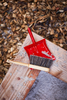 Red dustpan and broom on a wooden surface with wood chips in the background