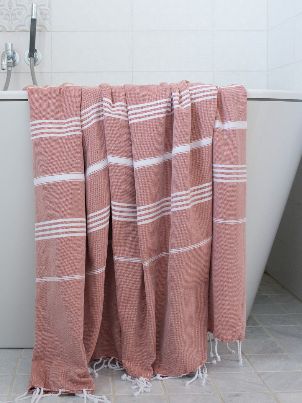 Pink towel with white stripes draped over a bathtub in a bathroom setting.