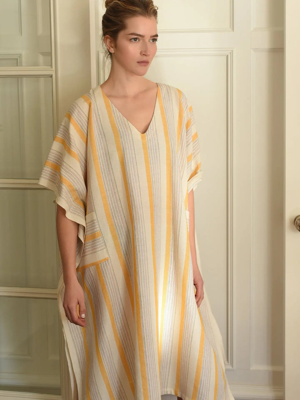 Woman wearing a striped dress with yellow and beige colors against a neutral background