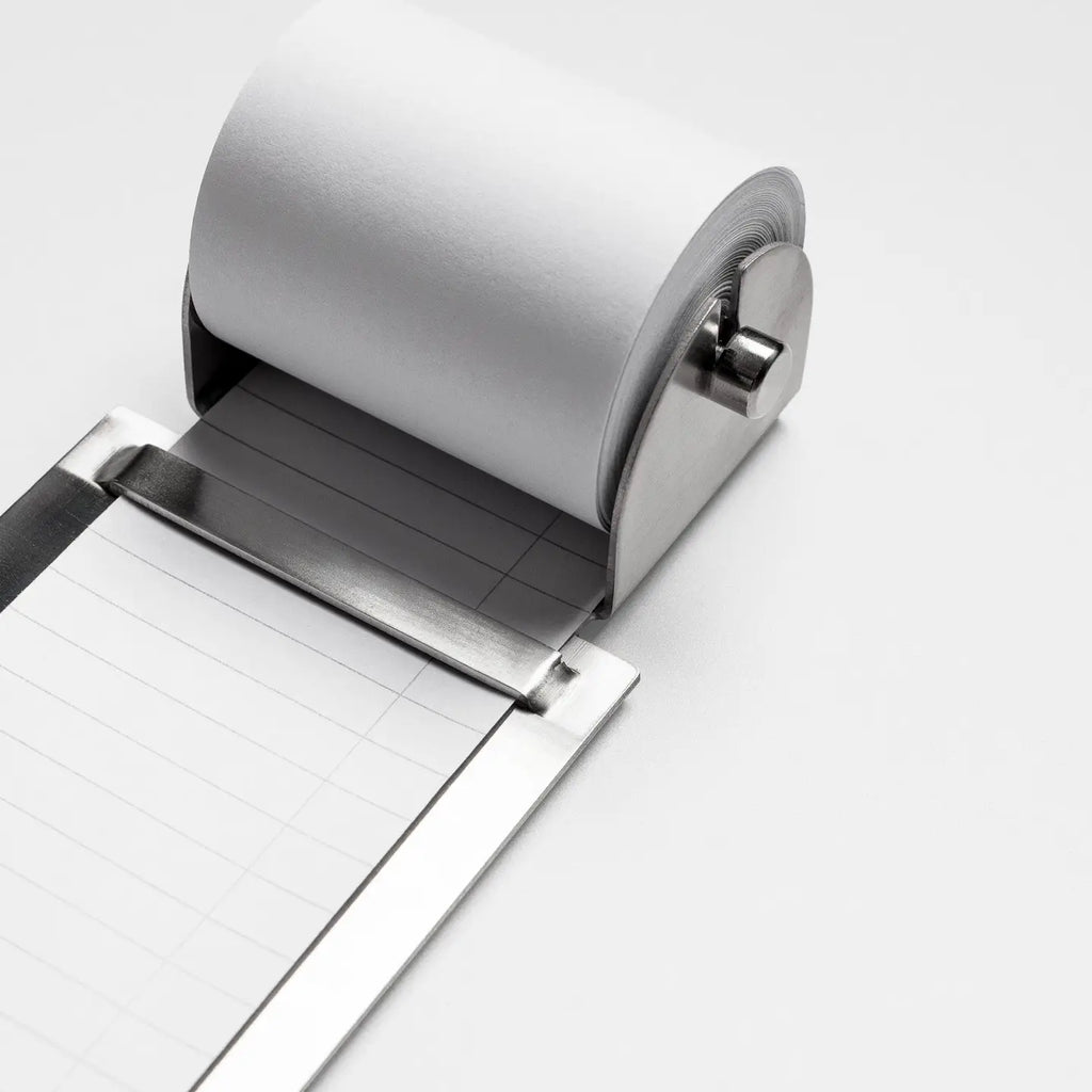 A close-up of a metallic roll of lined paper unspooling from a silver metal dispenser on a clean white background.