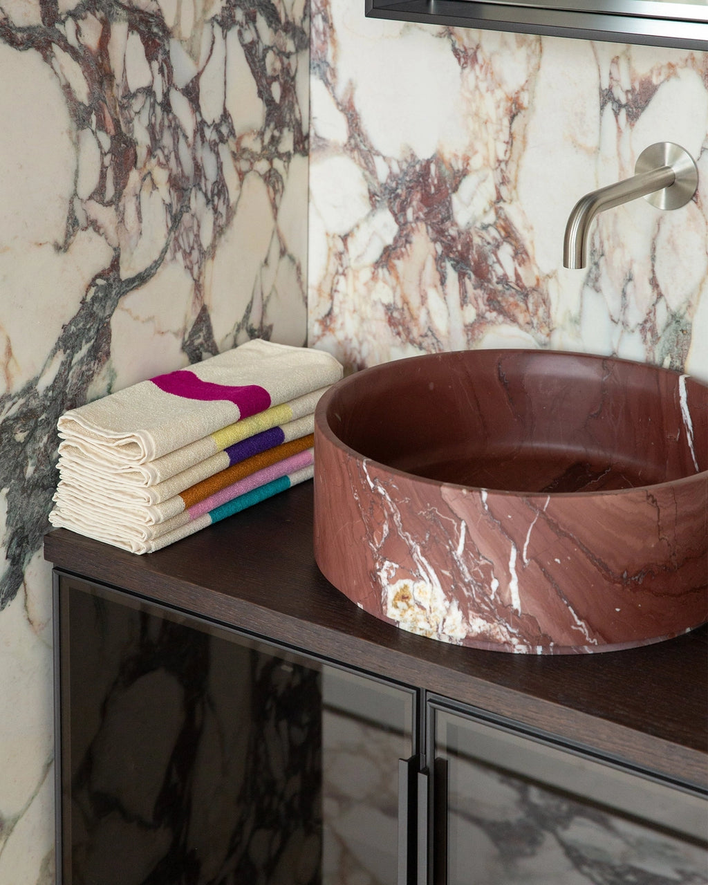 Marble-patterned sink and towels on a vanity with marble walls.