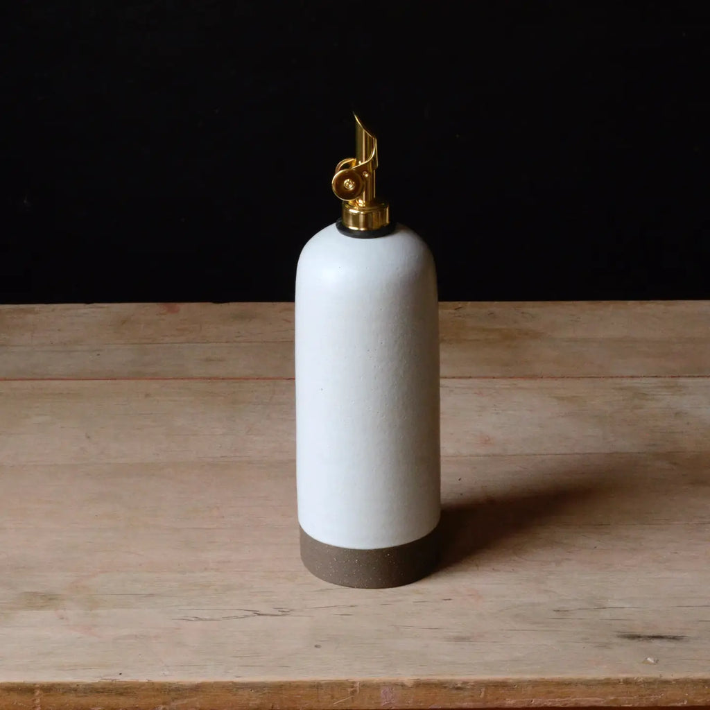 White ceramic oil bottle with gold cap on a wooden surface