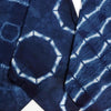 A close-up of dark indigo blue fabric with a white shibori tie-dye pattern, showing geometric hexagonal and grid-like markings.