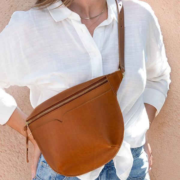 Person wearing a white shirt with a brown leather bag over the shoulder against a beige background