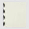 A cream-colored spiral-bound notebook with a black wire coil binding, shown from a top-down view on a light gray background.