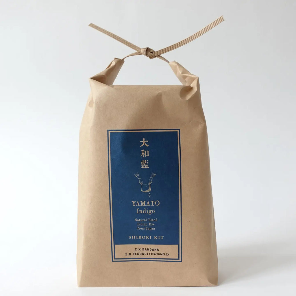 A kraft paper bag package tied with a thin ribbon at the top, featuring a blue front label with Japanese text and the English brand/product name Yamato Indigo.
